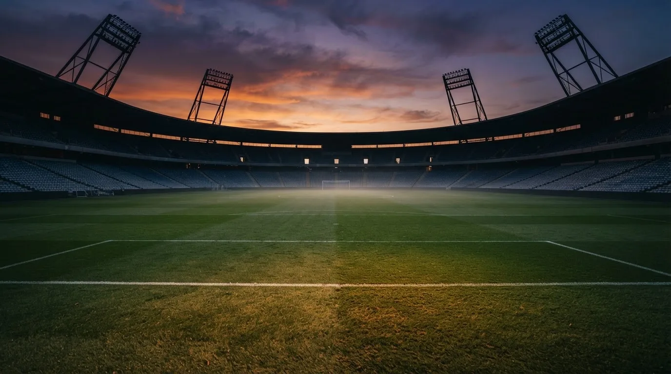 Un estadio de fútbol vacío con torres de iluminación al atardecer